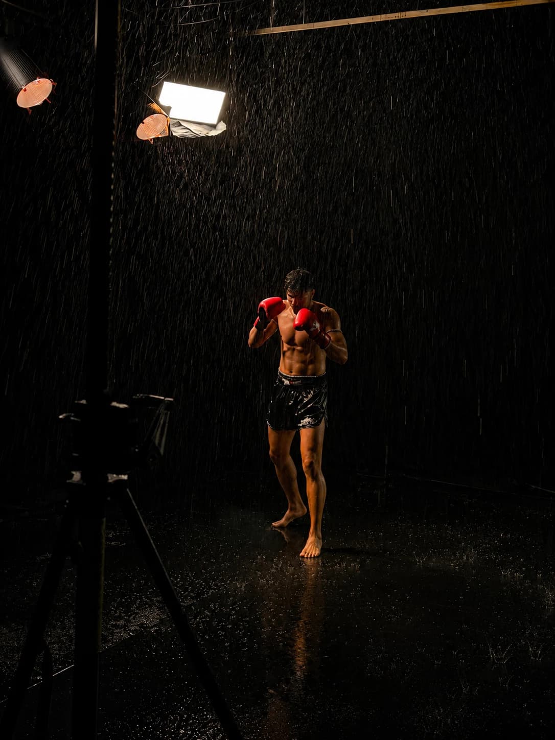 Combattant de Muay Thai gants aux poings sous la pluie, éclairé par un projecteur dans une ambiance sombre et cinématique