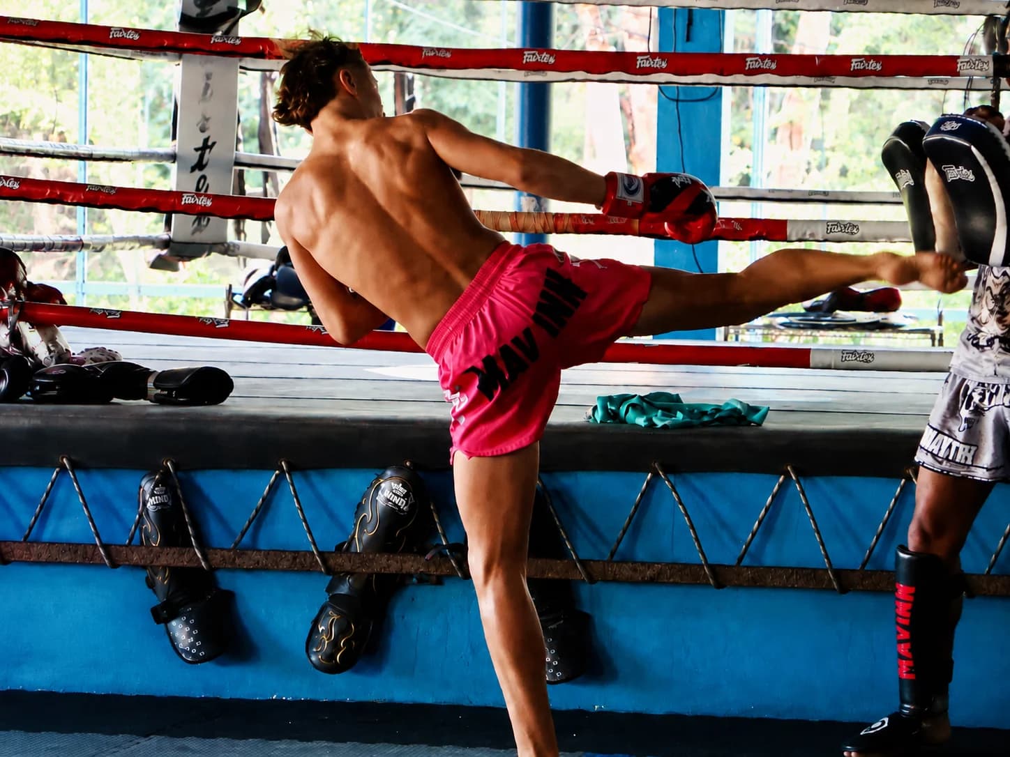 Combattant de Muay Thai décochant un coup de pied sur des pattes d'ours à l'entraînement sur le ring de Yodyut Muay Thai à Koh Samui